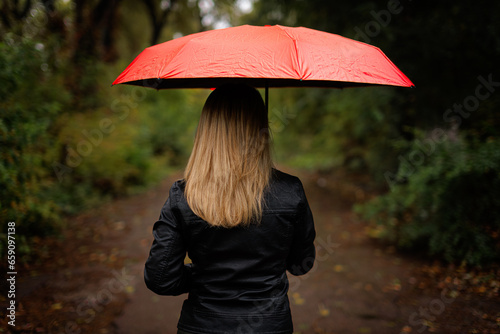 Silhouette of a girl from the back under an umbrella. A red umbrella in the fall