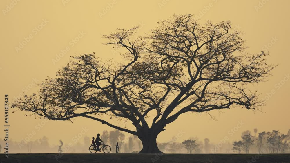 A lonely tree stands tall in the midst of a rural field, bathed in the golden light of dusk. The sky above is a canvas of orange hues. People gather beneath the tree, arriving on bicycles and on foot A lonely tree stands tall in the midst of a rural field, bathed in the golden light of dusk. The sky above is a canvas of orange hues. People gather beneath the tree, arriving on bicycles and on foot
