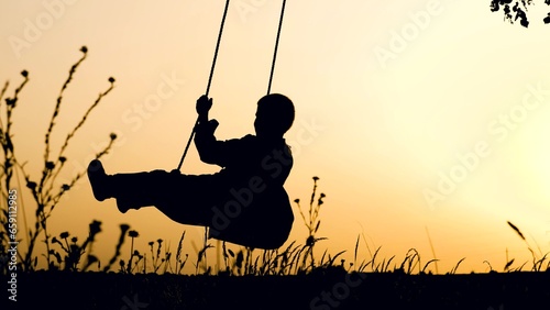 Playful little boy playing swings silhouette in rural park against sunset sky