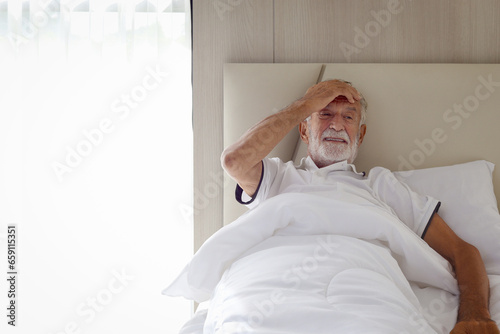 Male senior patient lying in hospital bed. Elderly man feeling sick need to rest in bed at home, ill upset man has a headache, puts hand on forehead because of pain. Elderly people health care concept