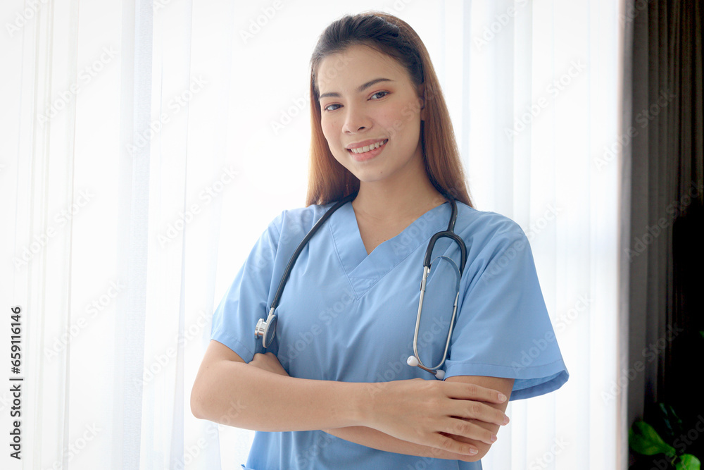 Portrait of happy smiling beautiful woman doctor with stethoscope in blue coat standing with arms crossed by window in clinic hospital. Female nurse on white background, medical health care worker. Portrait of happy smiling beautiful woman doctor with stethoscope in blue coat standing with arms crossed by window in clinic hospital. Female nurse on white background, medical health care worker.