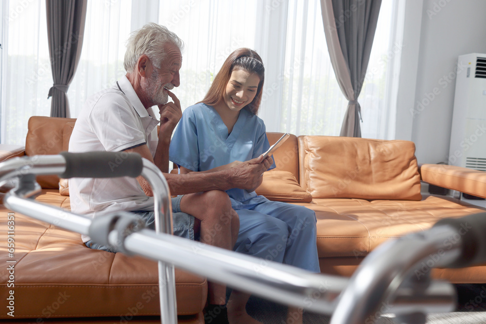 Fototapeta premium Female nurse takes care of senior patient and teaches him to use digital tablet at living room house, elderly mature grandfather learns to online internet and high-tech, nursing medical health care.
