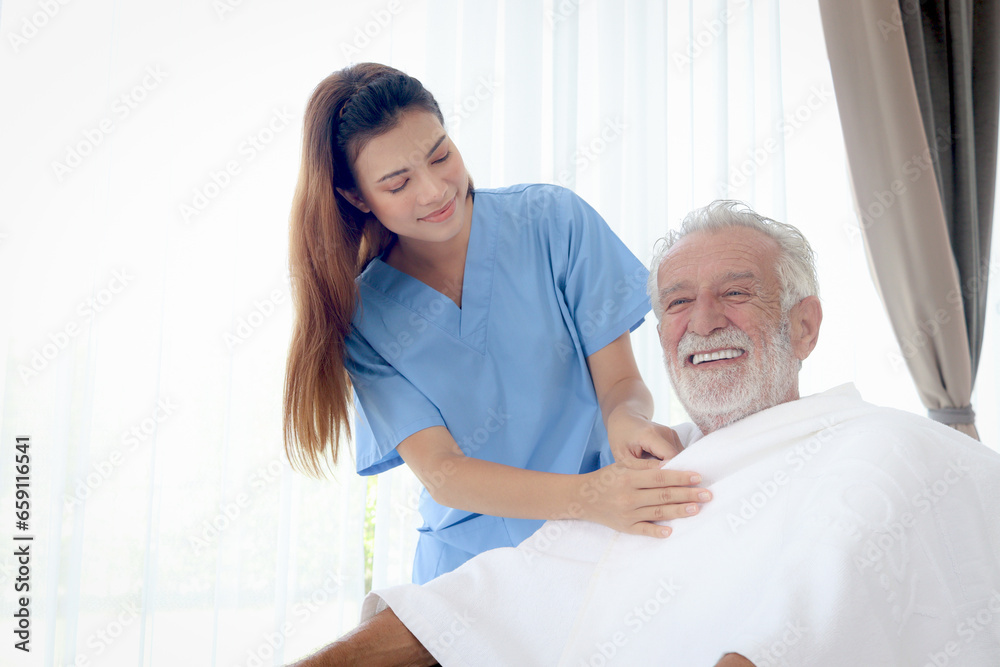 Obraz premium Beautiful female nurse takes care of senior patient in wheelchair at home, disabled elderly man sits in wheelchair while woman doctor covers blanket to mature grandfather, nursing medical health care.