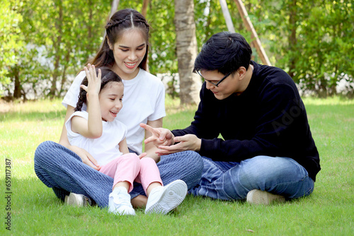 Happy family sitting on green grass, having fun and spending time together in summer garden, cute daughter girl sitting on mother lap during playing with her father at backyard. Family love bonding. © Stella