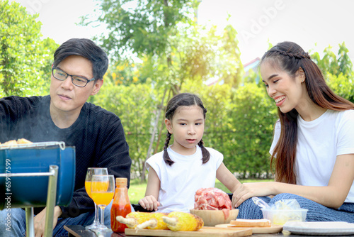Joyful parent and kid child make barbecue at picnic party  have fun together in summer green garden  father mother and daughter girl enjoy eating and drinking at backyard  happy family love bonding.