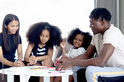 Happy family love bonding  African father mother and two daughter girls with curly hair enjoy spending time at home  little kids and parents make hand drawing paper craft card together in living room.