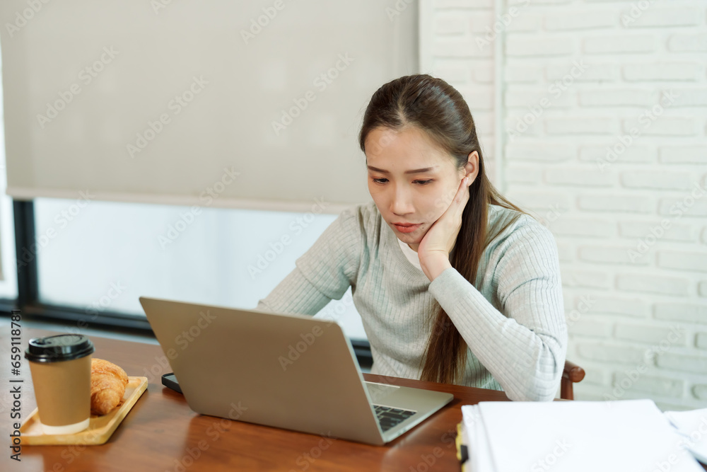 Beautiful young businesswoman, coffee shop owner, small business, beautiful Asian woman thinking about resting her cheeks while working on accounting documents on laptop. Boring at work Beautiful young businesswoman, coffee shop owner, small business, beautiful Asian woman thinking about resting her cheeks while working on accounting documents on laptop. Boring at work