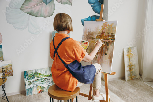 Foto Full body back rear view elderly artist woman 50 years old wearing casual clothes sitting near easel with painting artwork paint spending free spare time in living room indoor