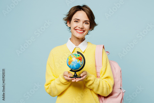 Young smiling happy woman student wear casual clothes yellow sweater backpack bag hold in hands globe Earth map looking camera isolated on plain blue background High school university college concept