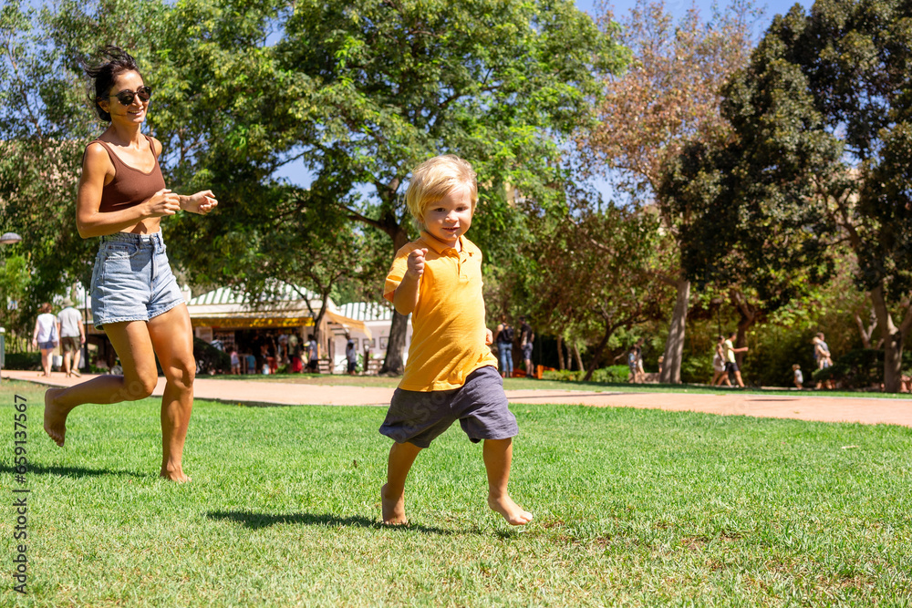 mother and little son run in the park on the green grass