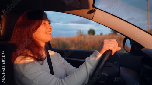Cheerful young woman drives modern car along rural road at sunset light © Валерий Зотьев
