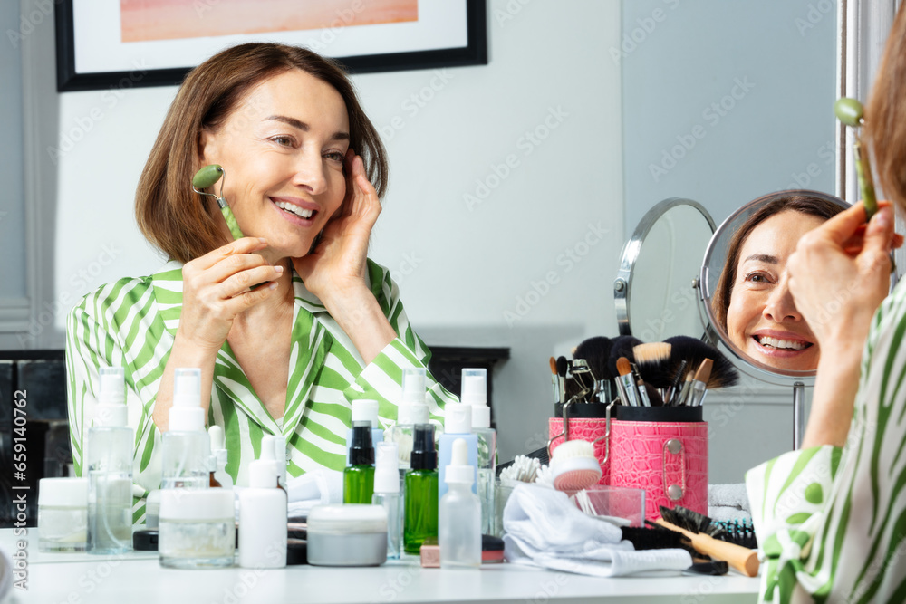 Woman uses facial roller for skincare before bathroom mirror Woman uses facial roller for skincare before bathroom mirror