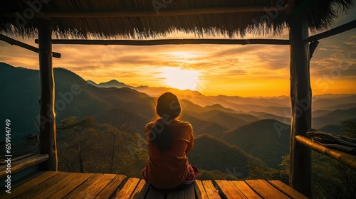 Picture from the back of a woman sitting on wooden porch extending into a high mountain cliff