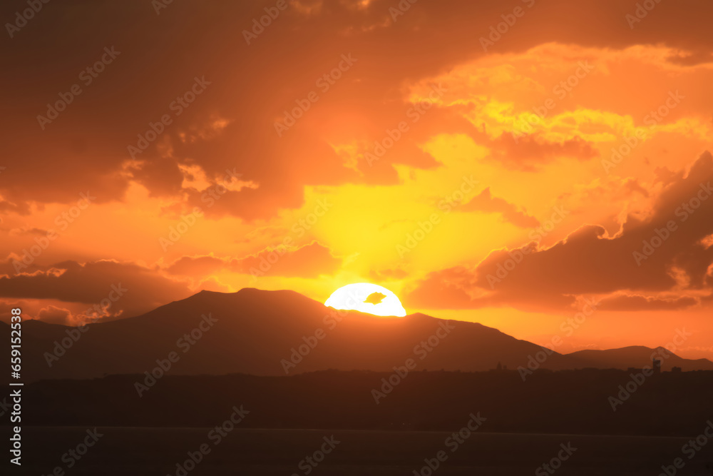 a sunset with a mountain in the background and clouds in the sky above it