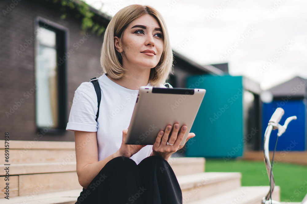 Thoughtful adult modern female sitting on stairs with bicycle browsing tablet in street Thoughtful adult modern female sitting on stairs with bicycle browsing tablet in street