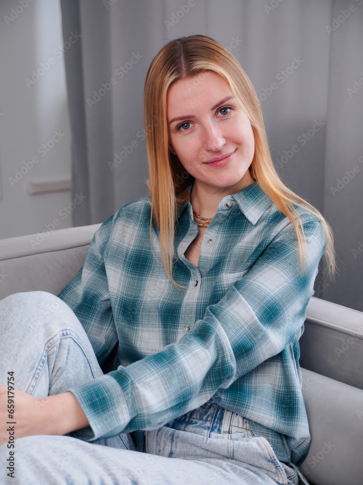 Fototapeta premium Beautiful woman blonde with natural makeup wear fashion clothes. Female cozy comfort sitting in cozy clean modern living room at home.