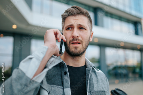 A young bearded man appears upset as he engages in a phone conversation in the city. Angry Man with Mobile Phone, Deep in Conversation, Looking Sad