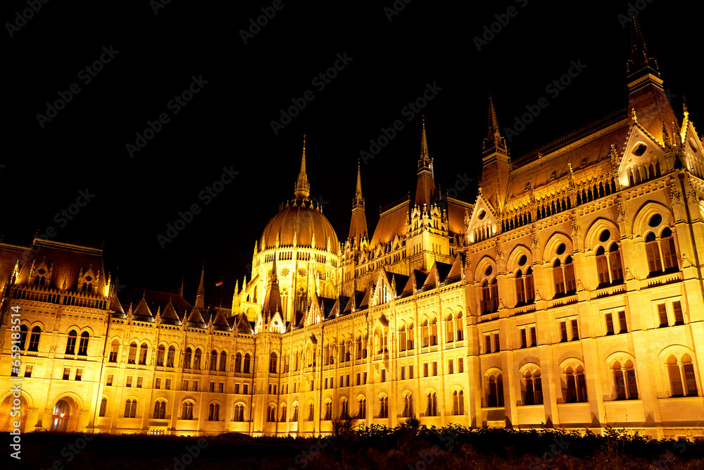 Evening photo of the Parliament building in Budapest. The majestic Saxon architecture is illuminated with warm yellow light