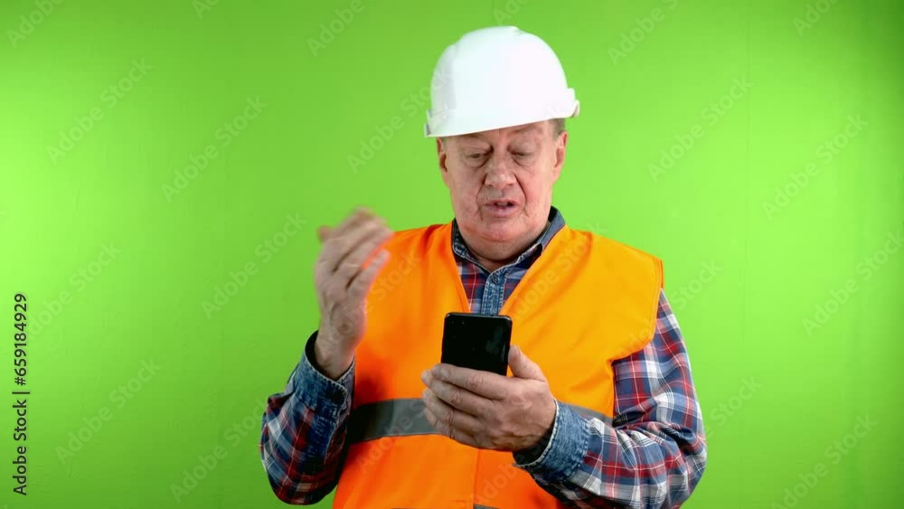 Senior builder in hardhat talking with phone webcam talking about things at work. Senior builder in hardhat talking with phone webcam talking about things at work.