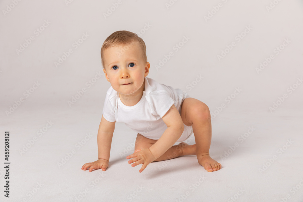 Happy laughing screaming toddler baby in diaper and white bodysuit is crawling on all fours looking at upper corner over white background. Happy infancy and babyhood concept Happy laughing screaming toddler baby in diaper and white bodysuit is crawling on all fours looking at upper corner over white background. Happy infancy and babyhood concept