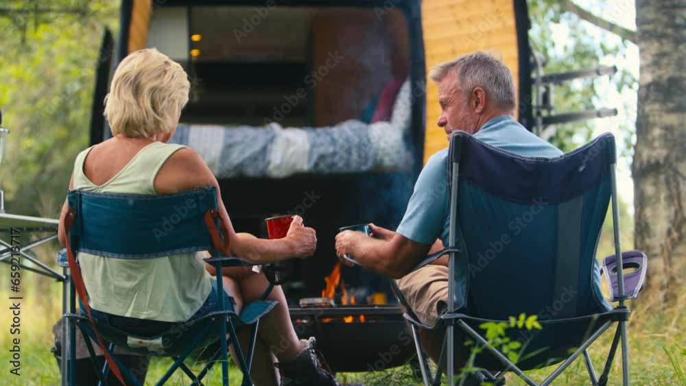 Rear view of senior couple camping in countryside with RV drinking coffee by outdoor fire - shot in slow motion Rear view of senior couple camping in countryside with RV drinking coffee by outdoor fire - shot in slow motion