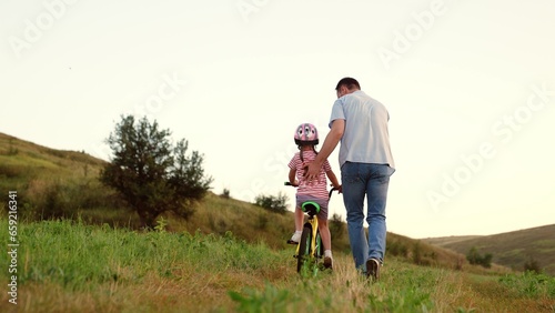 Supportive father takes care of preschooler girl learning to ride bicycle in field