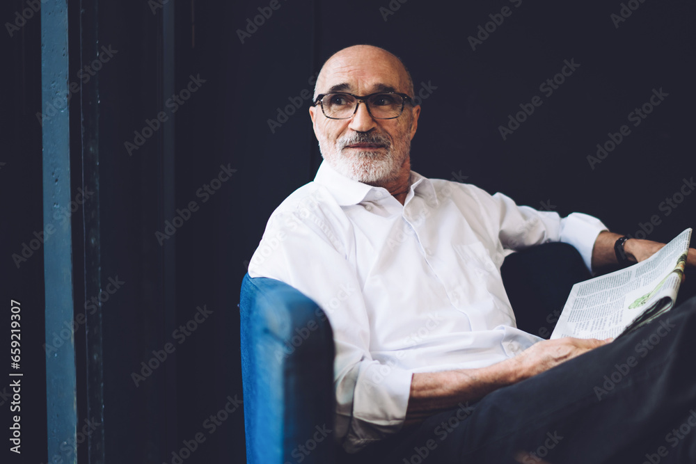 Thoughtful old bald male in eyeglasses reading newspaper siting in cafe Thoughtful old bald male in eyeglasses reading newspaper siting in cafe