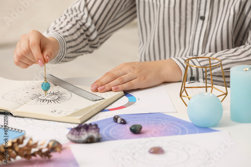 Astrologer using zodiac wheel and pendulum for fate forecast at table, closeup. Fortune telling photo
