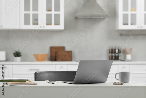 Home office. Laptop, glasses, smartphone and cup on white desk in kitchen, space for text