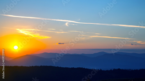 Colorful clouds in the sky at sunset against the backdrop of a mountainous forest area.