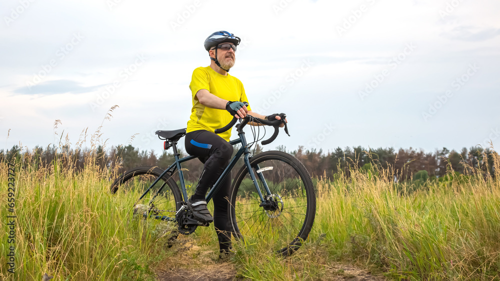 bearded man cyclist in yellow clothes is resting on a bicycle on the road in nature. sports, hobbies and entertainment for health