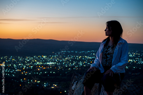 Woman on the mountain in profile looking at the beautiful colored sunset.