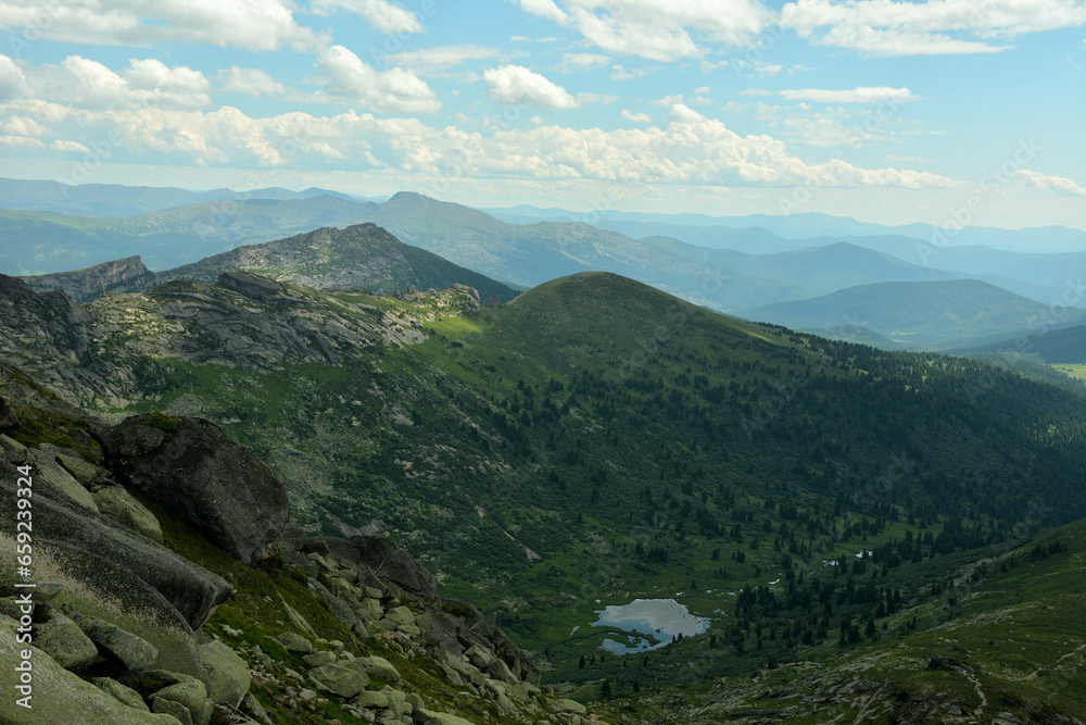 Fototapeta premium A view from the top to a small picturesque lake surrounded by high mountain ranges on a sunny summer day.