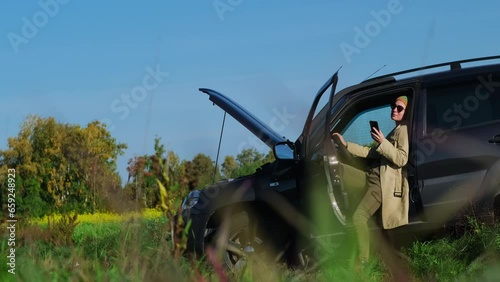 A frustrated female driver calling roadside service insurance. Road trip accident. Car breakdown drove into a ditch in a deserted countryside. photo