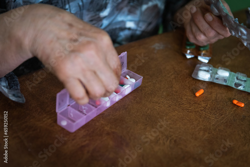 Close up shot of elderly woman organizing medicinal pills in a pill box at home.