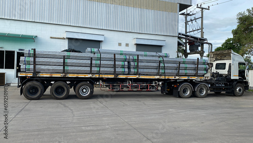 Trucks with long trailers carrying steel bars for building construction. Construction steel is ready to be delivered to the customer.