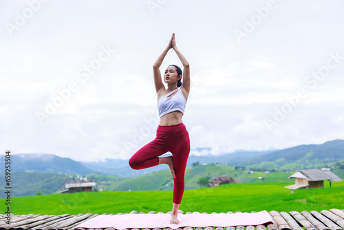 young girl is doing yoga on balcony of resort with rice terraces, Ban Pa Bong Piang and mountains green over white sky in rainy season, Travel healthy lifestyle, enjoying in nature concept,