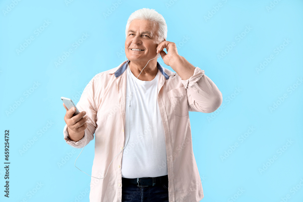 Senior man in earphones with mobile phone on blue background Senior man in earphones with mobile phone on blue background