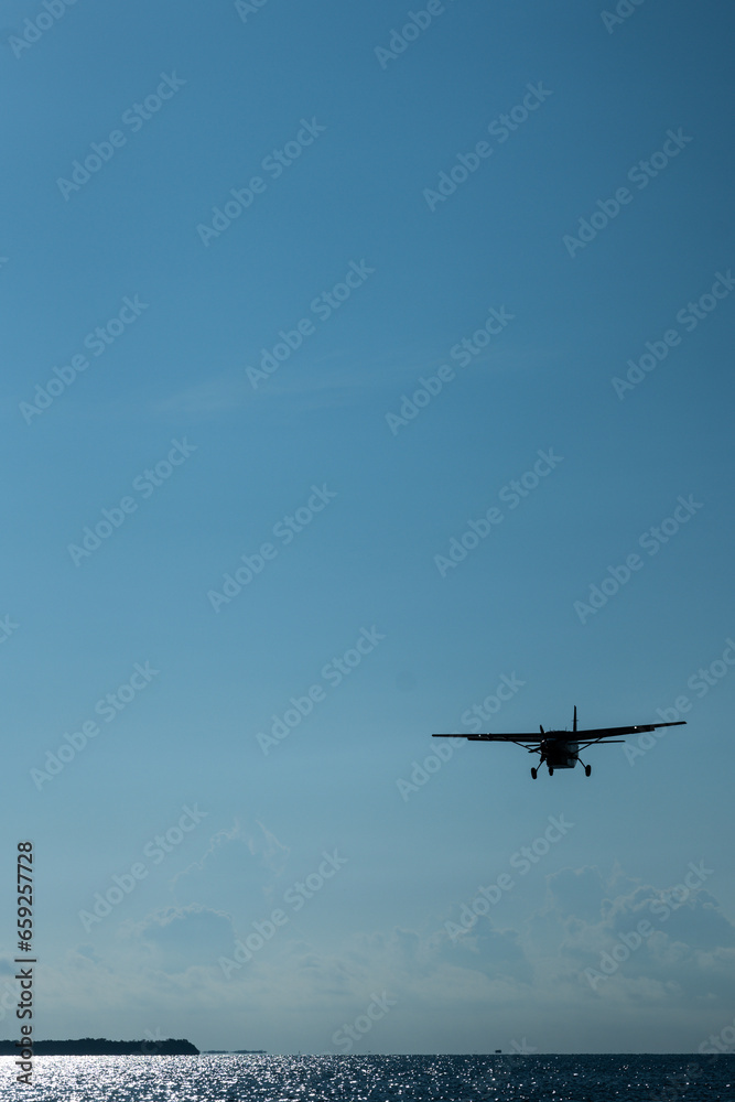 A propeller-driven plane flying over the sea with the sun at its back A propeller-driven plane flying over the sea with the sun at its back