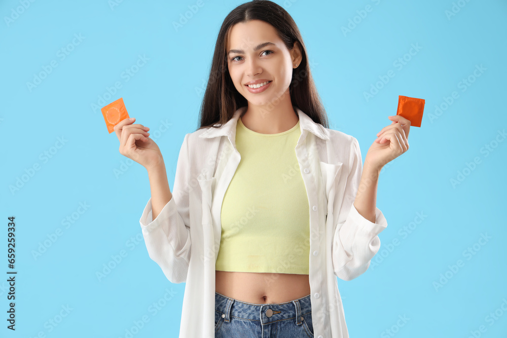 Young woman with condoms on blue background - obrazy, fototapety, plakaty 
