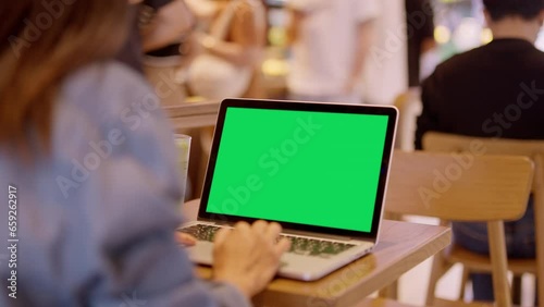 Over the shoulder shot of woman, using finger with keyboard for typing touch. computer laptop with blank green screen chroma key in cafe.