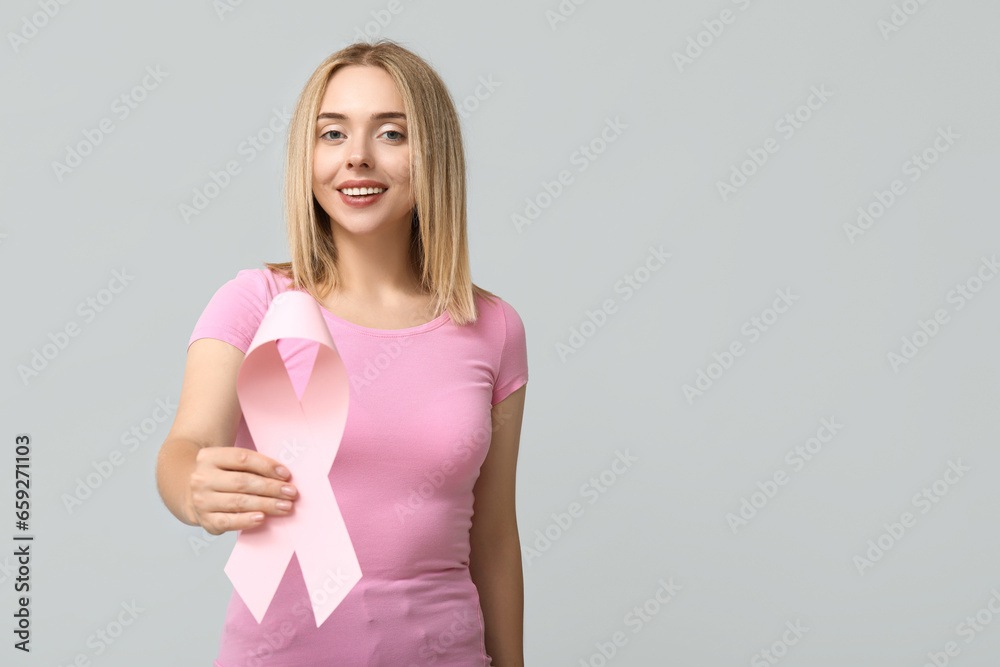 Young woman with pink ribbon on grey background. Breast cancer awareness concept Young woman with pink ribbon on grey background. Breast cancer awareness concept