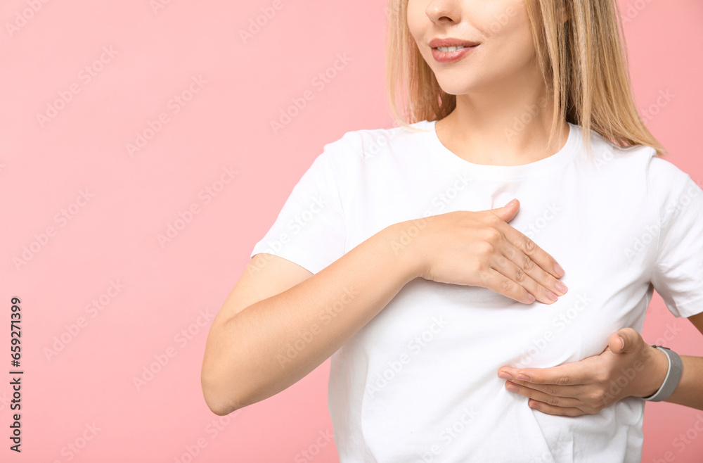 Young woman checking her breast on pink background. Cancer awareness concept Young woman checking her breast on pink background. Cancer awareness concept