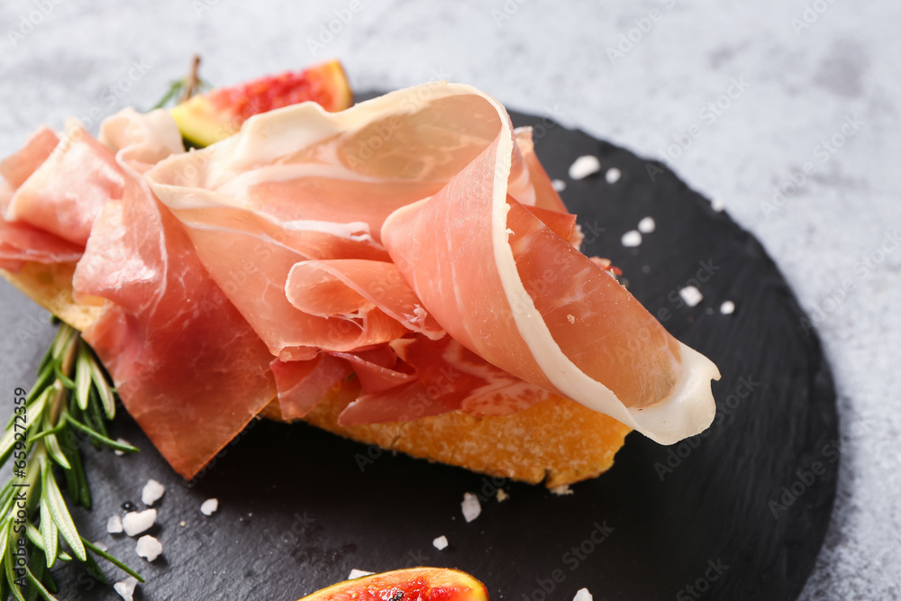 Board of tasty sandwich with prosciutto on grey background