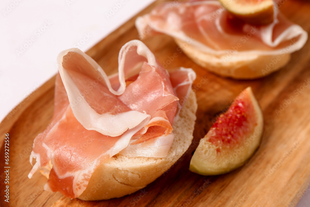 Wooden board with of tasty sandwiches with prosciutto on white background