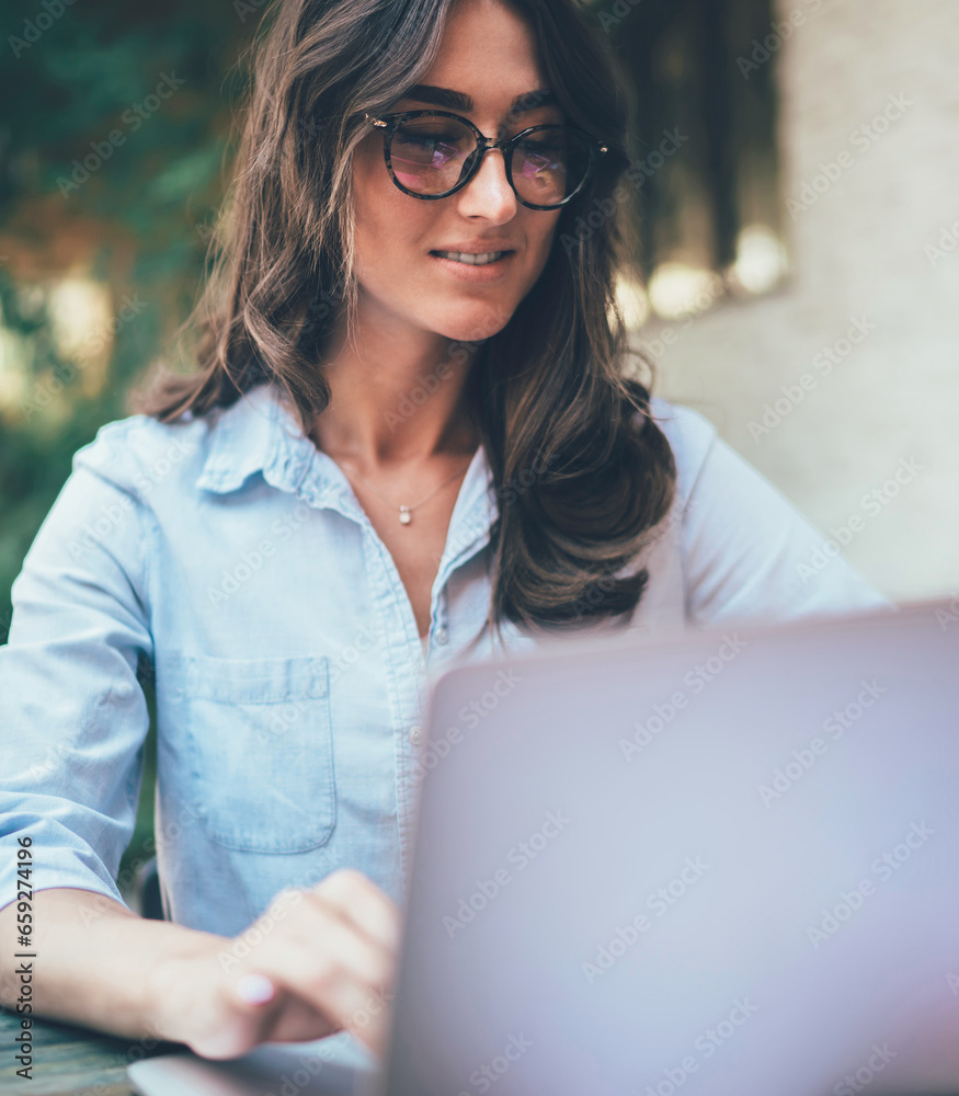 Attentive adult businesswoman comparing information in documents while using laptop on cafe terrace Attentive adult businesswoman comparing information in documents while using laptop on cafe terrace