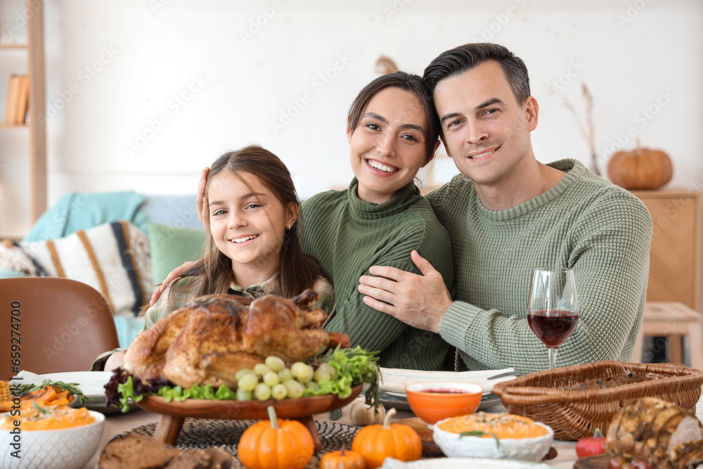 Little girl with her parents having dinner at festive table on Thanksgiving Day