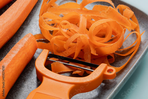 Φωτογραφία Close view of a blue plate with carrots, carrot peels and a peeler tool on light