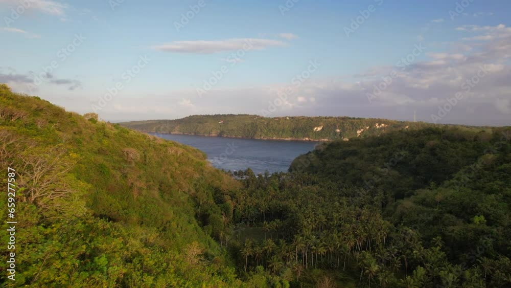 Aerial Flying Close to Rainforest Trees in a Valley at Sunrise with a View of Gamat Bay Beach in Nusa Penida, Bali, Indonesia Aerial Flying Close to Rainforest Trees in a Valley at Sunrise with a View of Gamat Bay Beach in Nusa Penida, Bali, Indonesia
