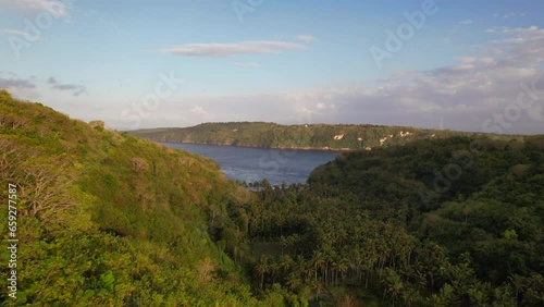 Aerial Flying Close to Rainforest Trees in a Valley at Sunrise with a View of Gamat Bay Beach in Nusa Penida, Bali, Indonesia photo